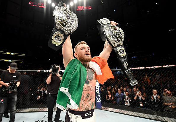 Conor McGregor poses with both of his belts after defeating Eddie Alvarez at UFC 205